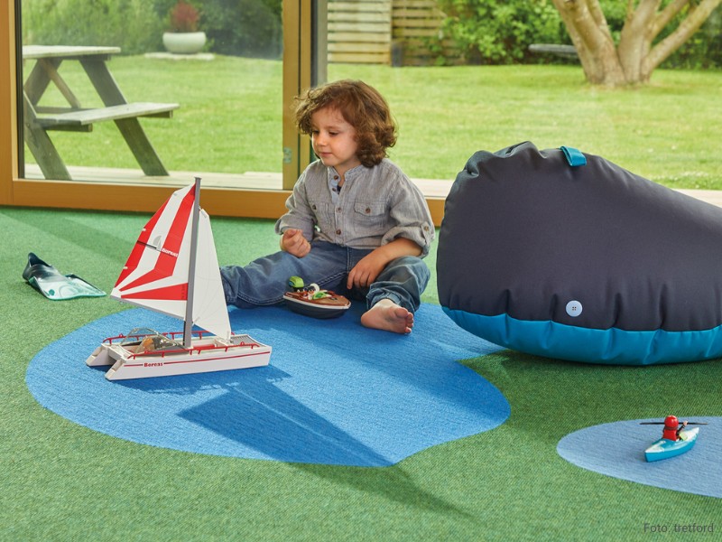 Kreative Gestaltung für das Kinderzimmer Kind spielt mit Segelboot auf dem kreativ gestaltenen Teppichboden